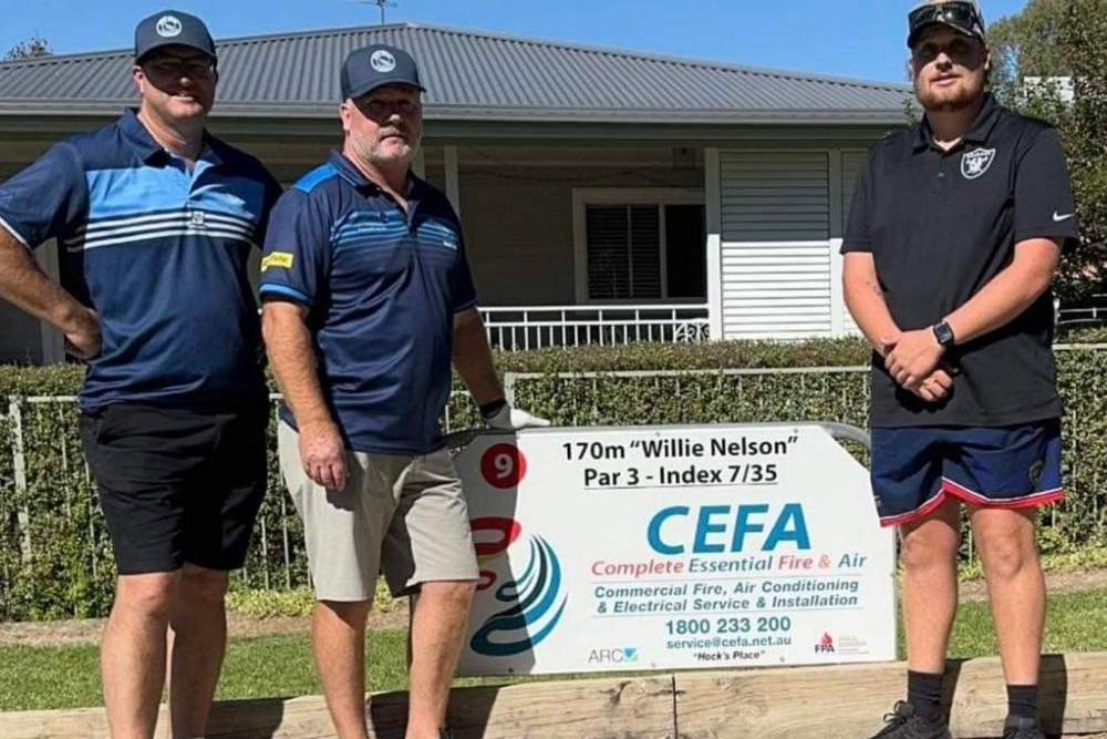 Three men standing beside a Complete Essential Fire and Air sign